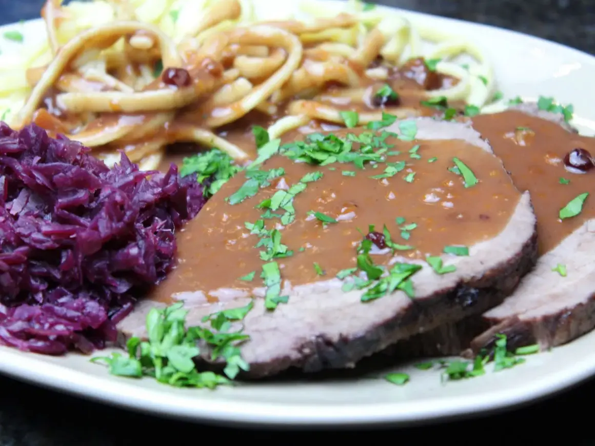 Sauerbraten mit Klößen und Rotkohl. Die Marinierzeit für Sauerbraten kann variieren, oft mehrere Tage.
