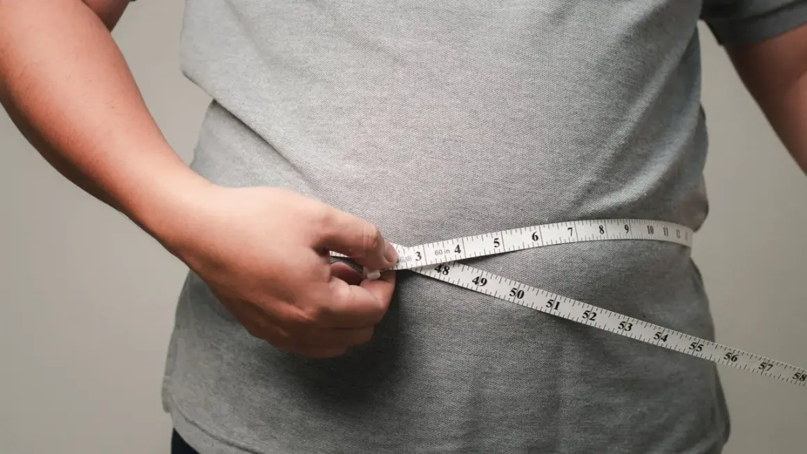 Person misst den Bauchumfang. Viele fragen sich, wo nimmt man zuerst ab – oft ist es der Bauch.