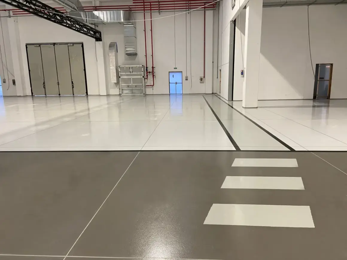 Pavimento industriale con finitura in resina epossidica, segnali di sicurezza e porte a libro.
