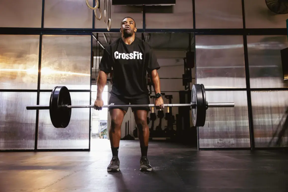 Mężczyzna w koszulce CrossFit podnosi sztangę na siłowni.