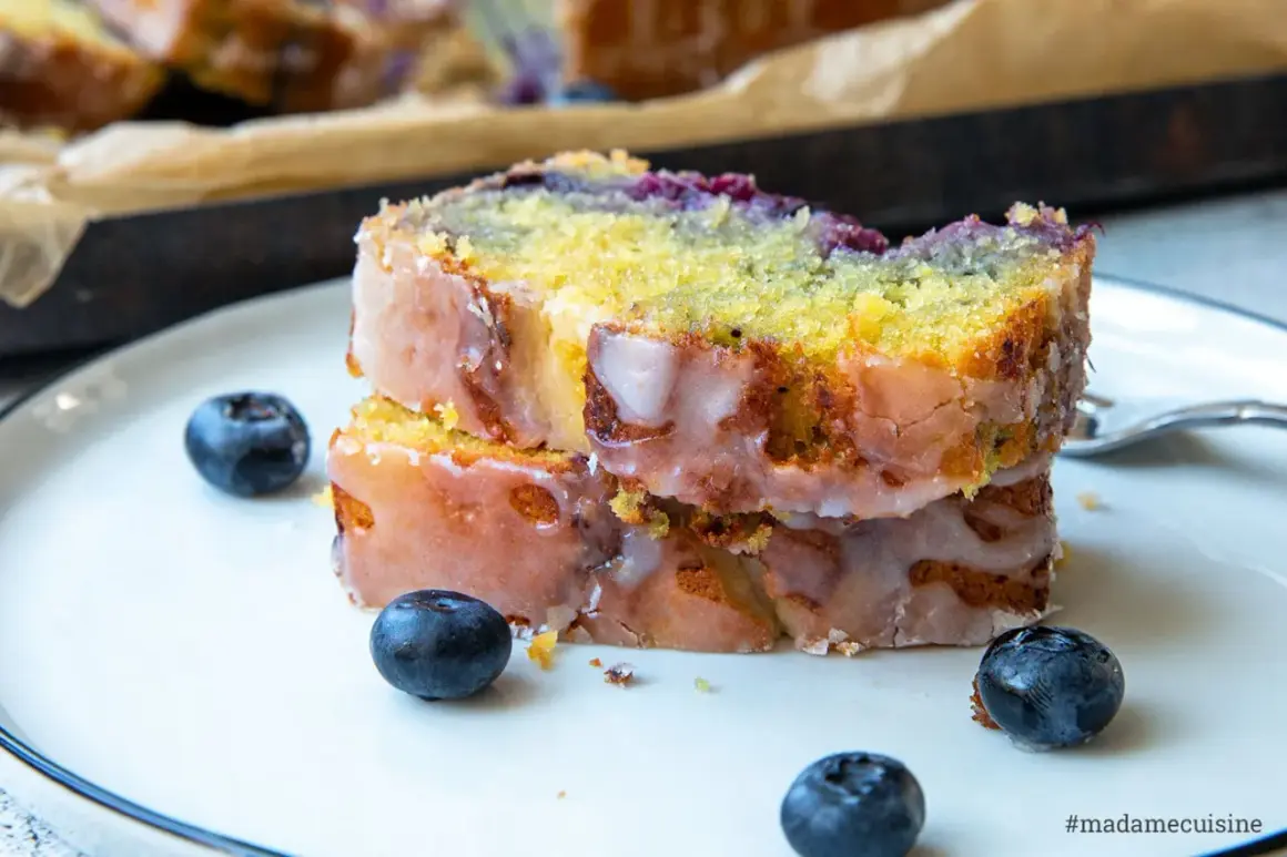 Zwei Scheiben saftiger zitronen blaubeer kuchen mit Zuckerguss und frischen Blaubeeren auf einem Teller.