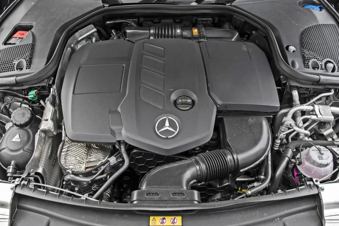 Silnik Mercedes-Benz E-Class. Widoczny czarny plastikowy dyfuzor, logo gwiazdy Mercedesa i elementy układu dolotowego.