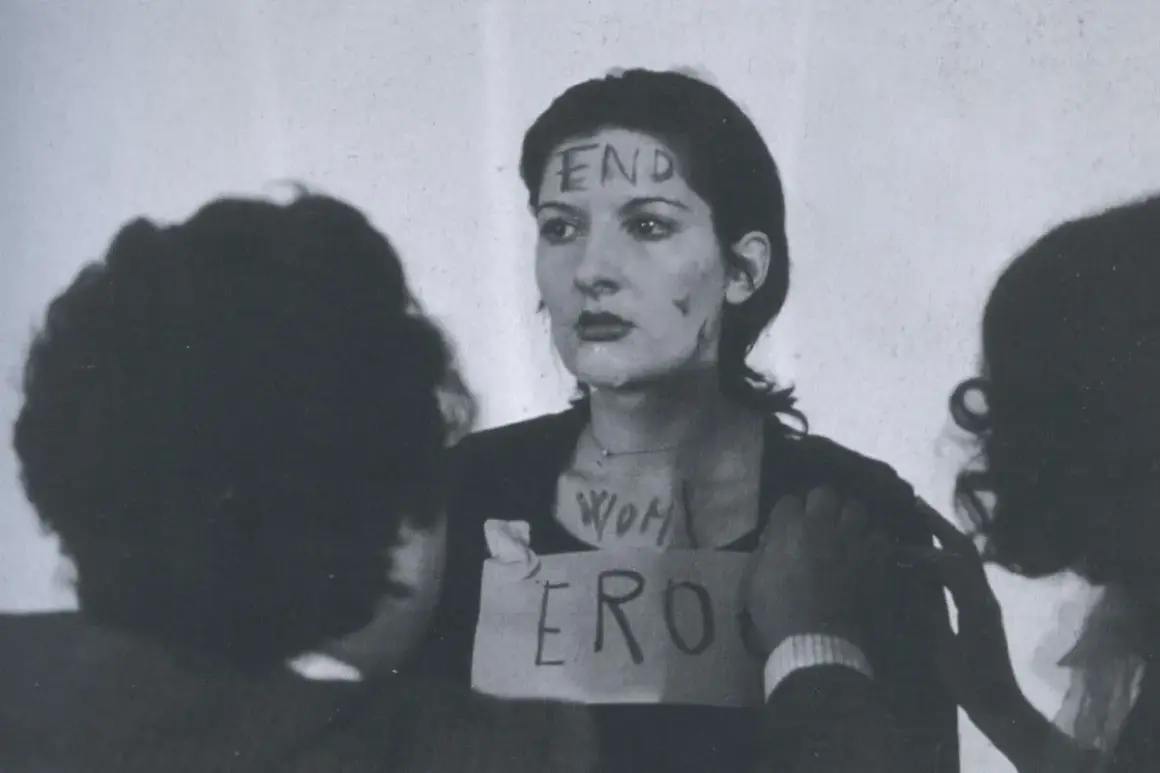Marina Abramović w performansie "Rhythm 0" z napisem "END" na czole i "WOMAN ERO" na klatce piersiowej.