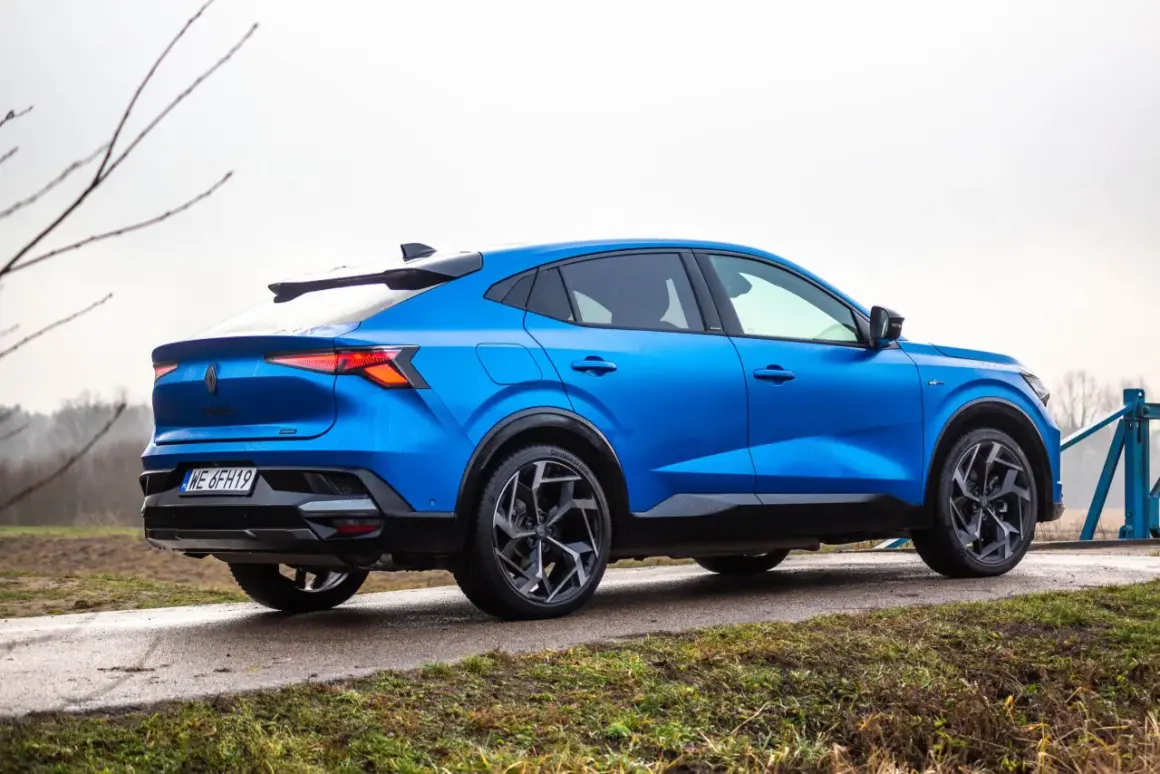 Niebieski Renault Rafale z dynamiczną linią dachu, zaparkowany na mokrej drodze.