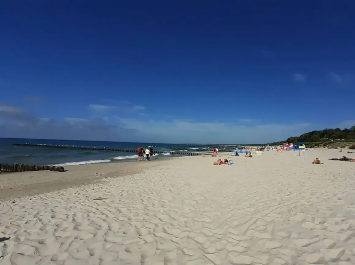 Słoneczna plaża wschodnia Ustka z ludźmi spacerującymi i odpoczywającymi na piasku.