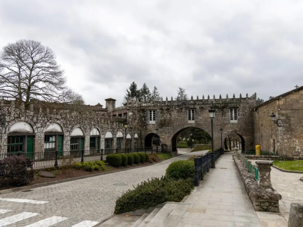 El Pazo de Coton, con su arquitectura de piedra y arcos, se alza bajo un cielo nublado, invitando a un paseo tranquilo.