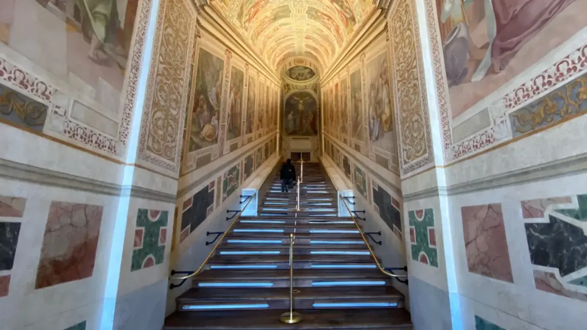 Persona subiendo la escalera santa de Roma, con frescos en las paredes y una crucifixión al final.