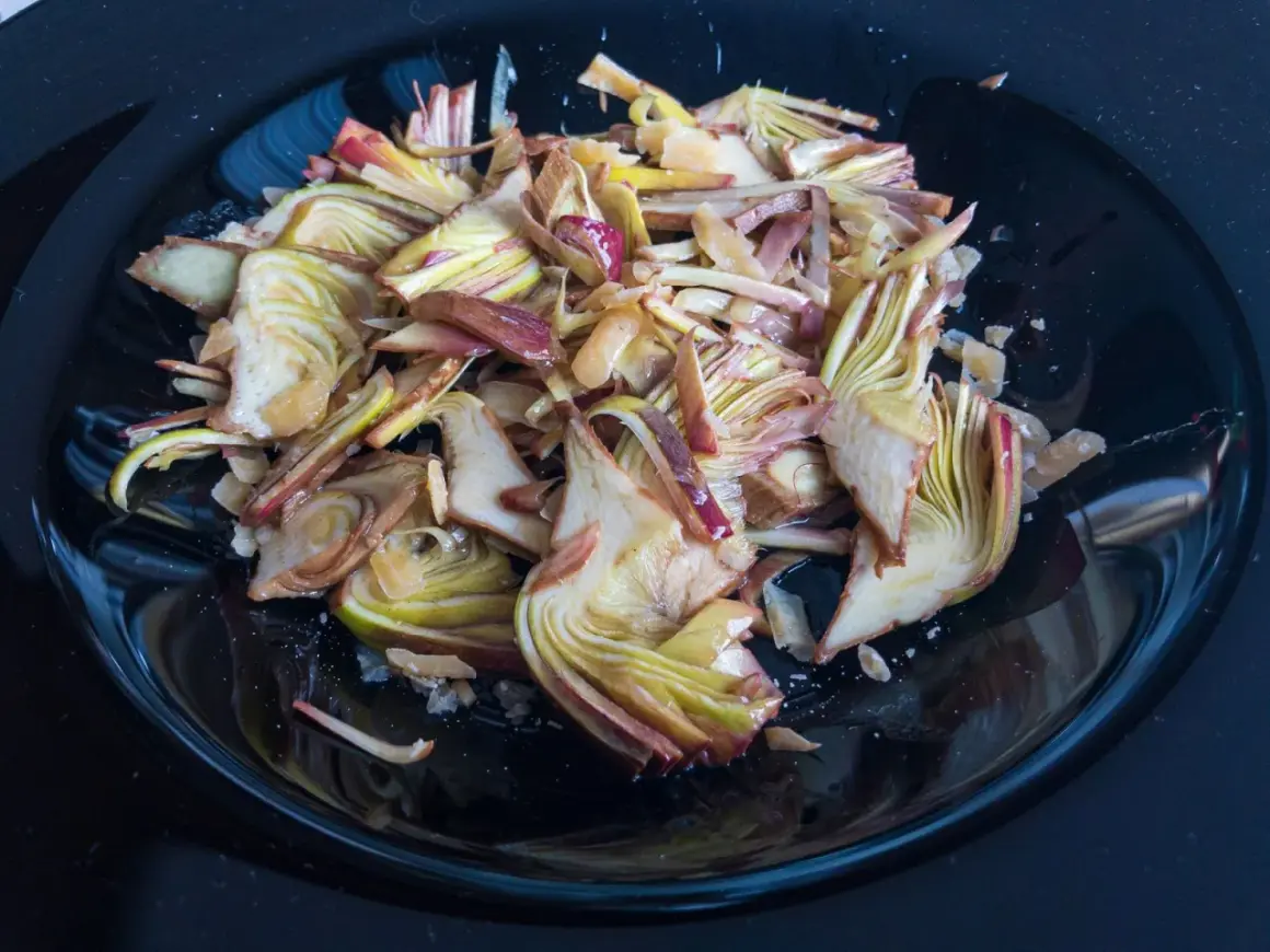 Un piatto nero lucido pieno di un'appetitosa insalata di carciofi crudi, tagliati finemente e conditi.