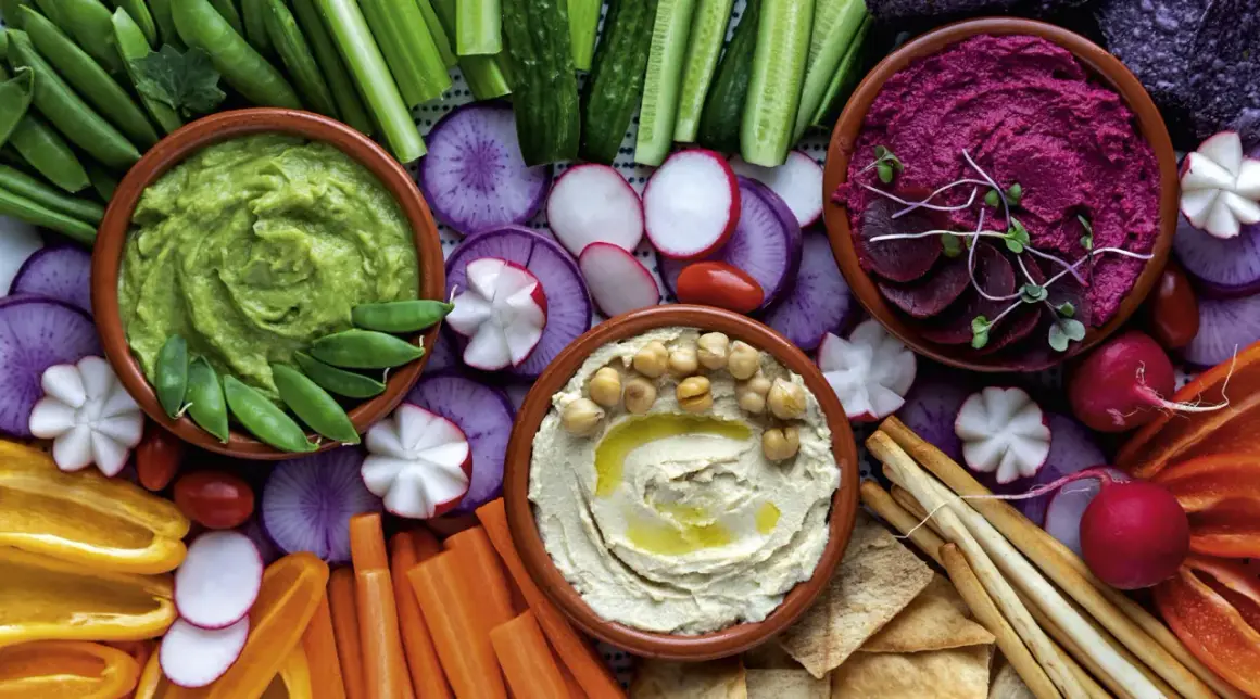 Bunte Auswahl an Dip-Rezepten: cremiger Hummus, grüner Avocado-Dip und Rote-Bete-Dip mit frischem Gemüse und Brot.