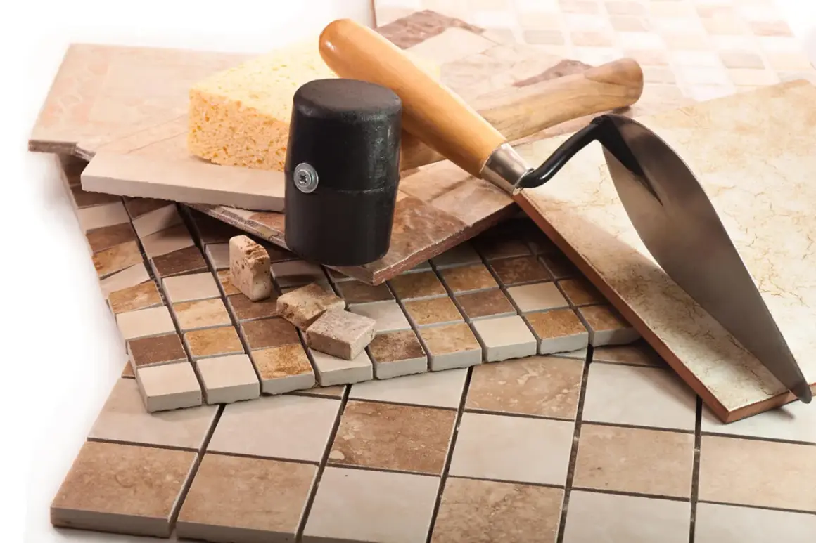 Diverses carreaux de céramique, une éponge, un maillet et une truelle, prêts pour une pose mosaïque sol.