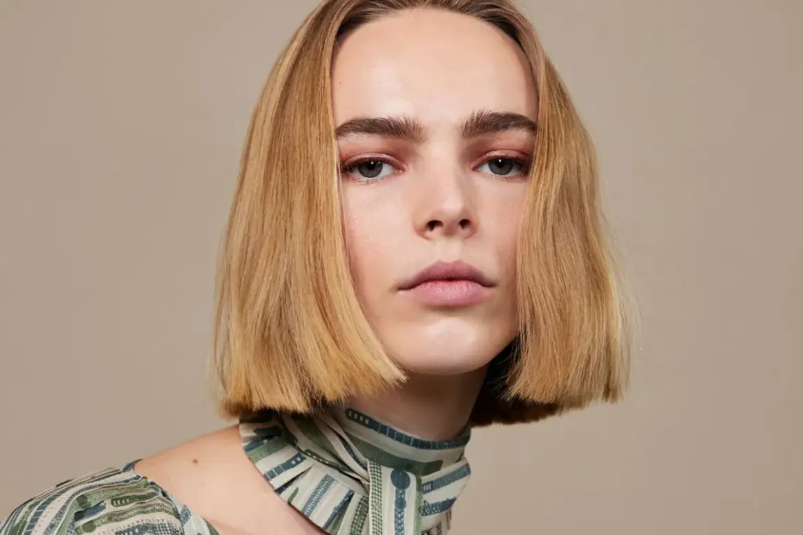 Modelka z idealnie prostymi, rudymi włosami w stylu blunt bob, z delikatnym makijażem oczu i ust, prezentuje się elegancko.