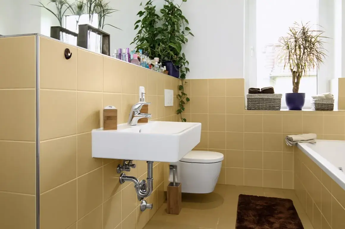 Bagno moderno con piastrelle color sabbia, lavabo sospeso, WC e vasca. Un'idea per dipingere piastrelle bagno con un tocco di calore.