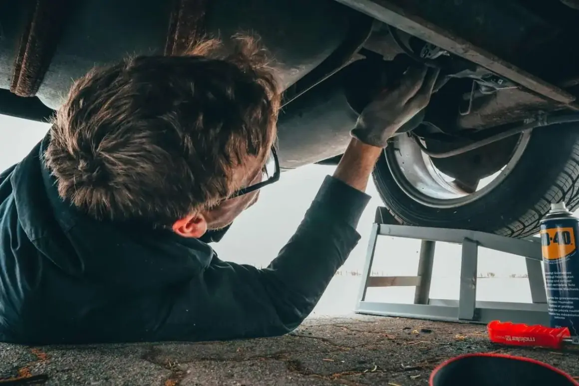 Mechanik podnosi auto sciaga na prawa strone, by naprawić podwozie. W tle puszka WD-40.