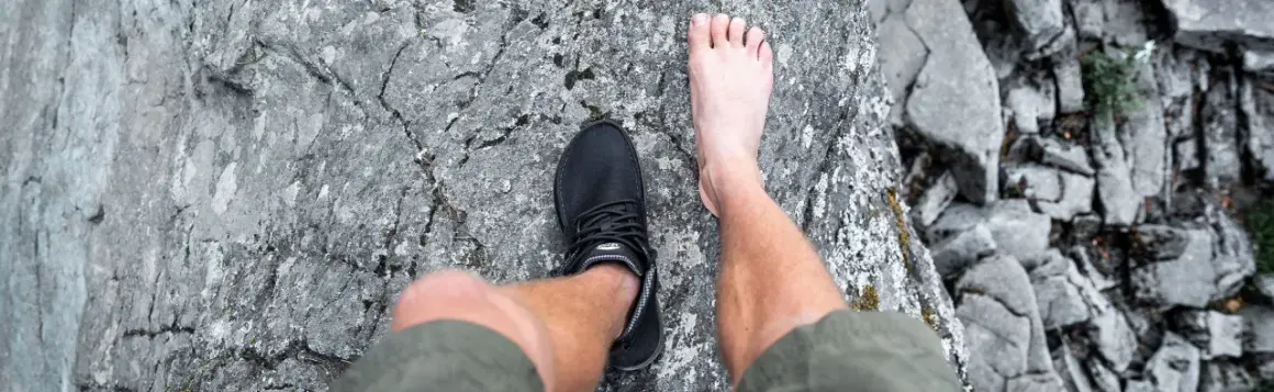 En barfota fot bredvid en barfotasko på en stenig yta. Frågan är om barfotaskor är bra eller dåligt för fötterna.