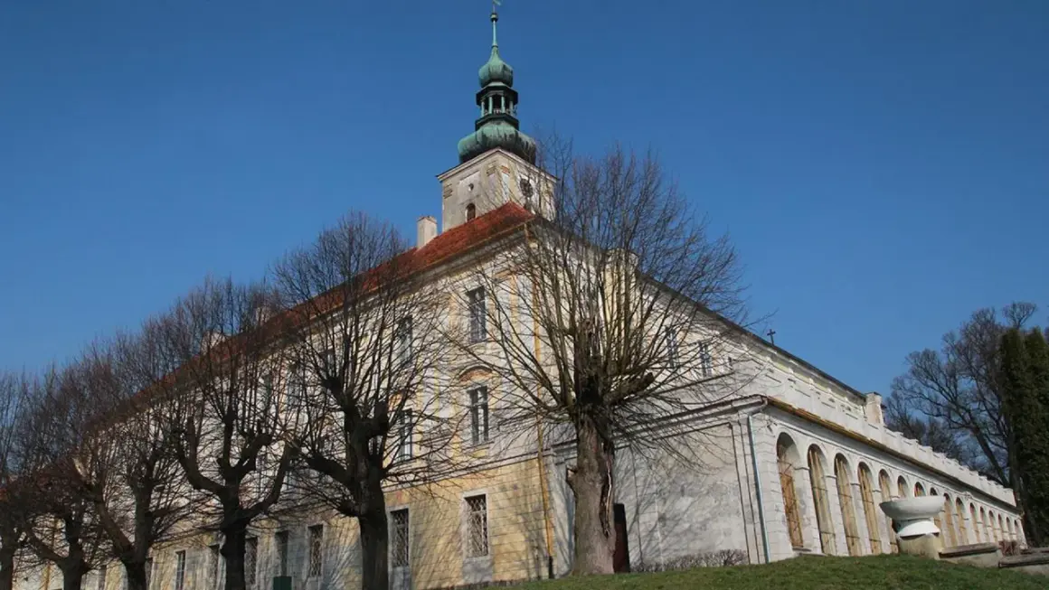 Dawny pałac w Oleśnicy Małej z charakterystyczną wieżą i arkadowym krużgankiem, otoczony nagimi drzewami.