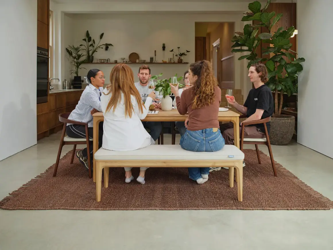 Friends enjoy drinks around a wooden table, showcasing a stylish mix and match of dining chairs and a bench for a relaxed gathering.