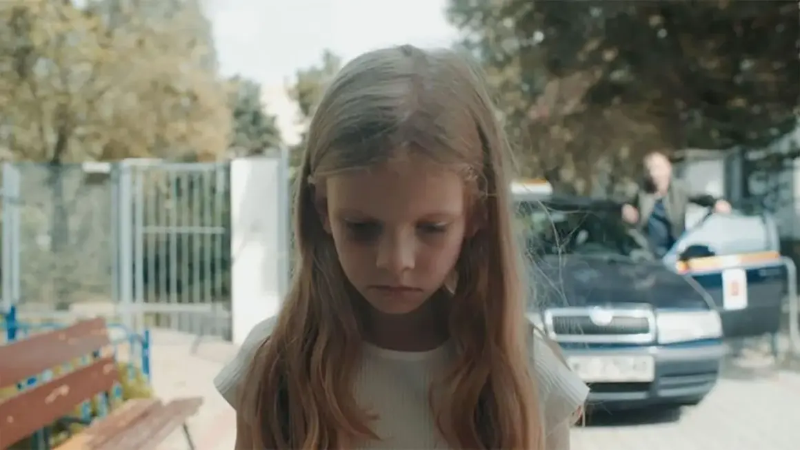 Smutna dziewczynka z sińcami pod oczami, w tle samochód i mężczyzna. Scena z filmu budząca konfuzję.