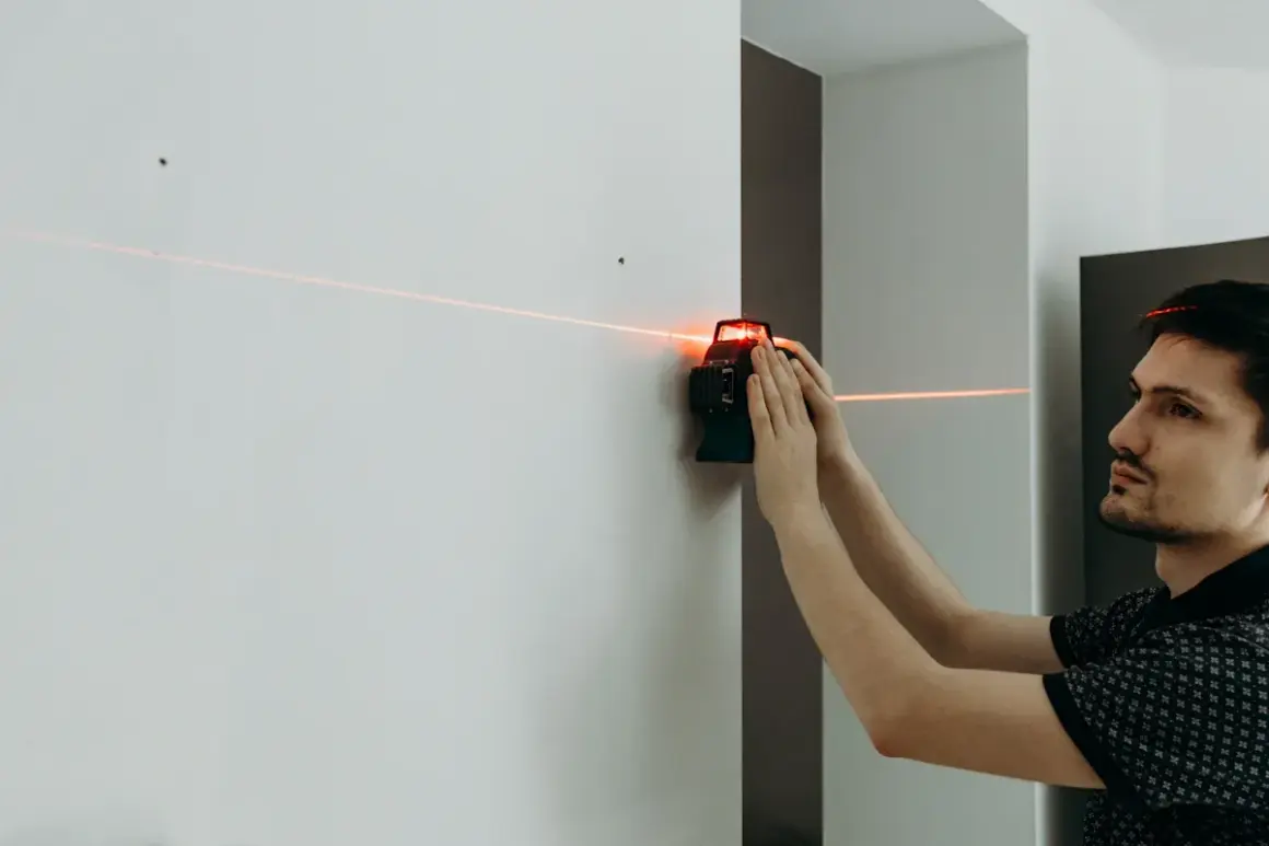 Un homme utilise un niveau laser pour tracer une ligne parfaitement droite sur un mur blanc.