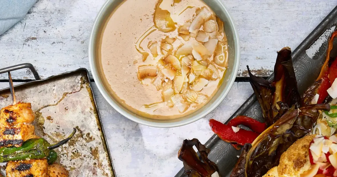 En krämig tahini-sås med kokosflingor, bredvid grillspett med kyckling och grönsaker samt ugnsbakad aubergine och paprika.
