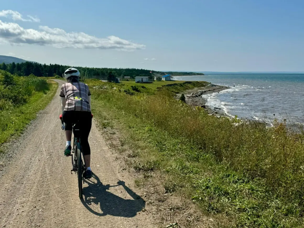 Rowerzystka na leśnych trasach rowerowych, podziwiająca widok na morze i domki na wybrzeżu.