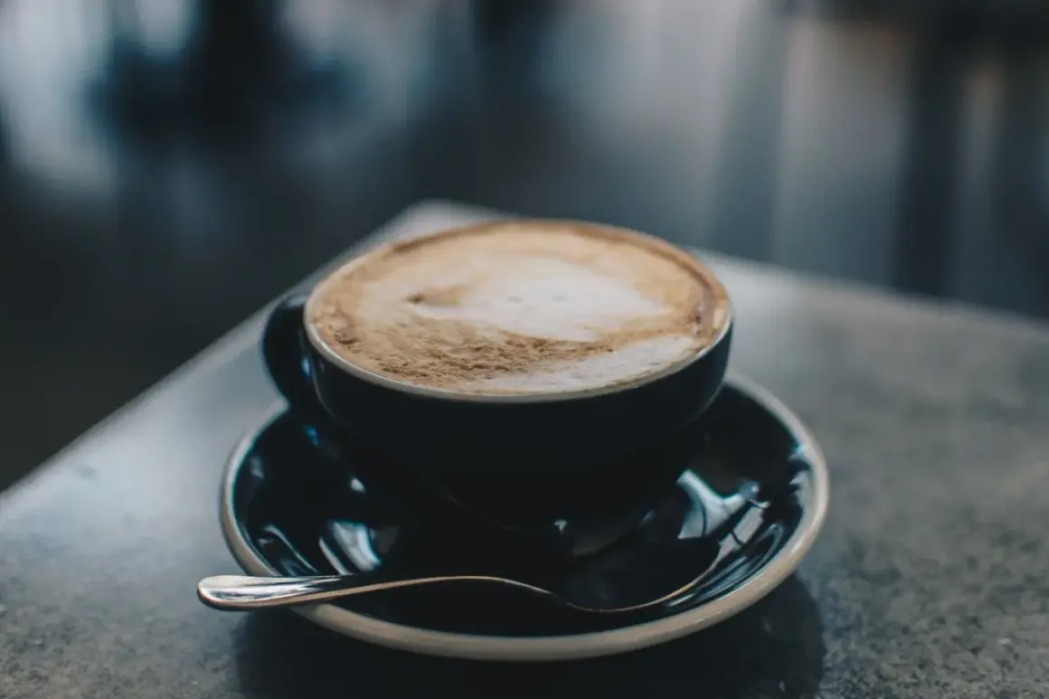 En kopp cappuccino med lattekonst, en av många italienska kaffesorter, står på ett fat med en sked.