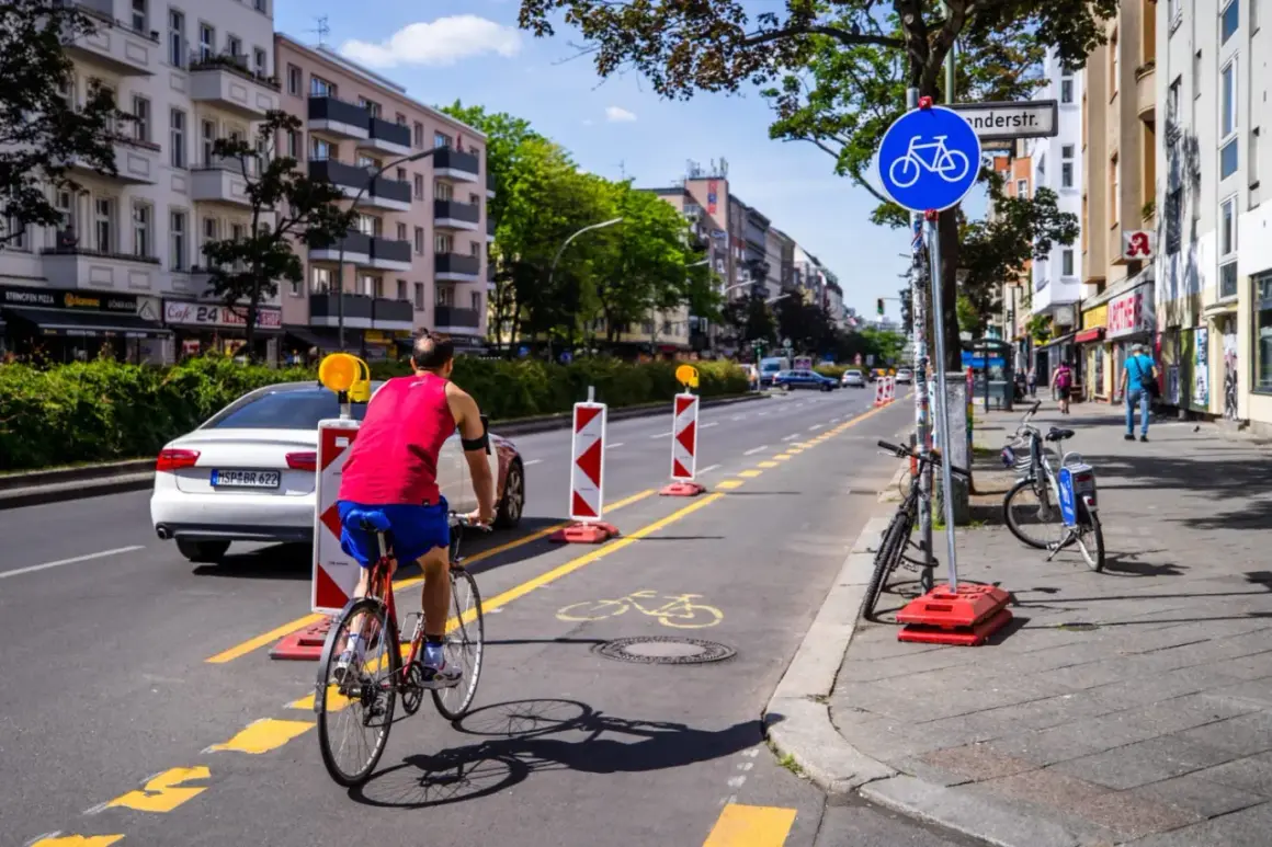 Ein Mann fährt auf einem pop-up Radweg in Berlin. Absperrungen markieren den Weg, der von Autos und Gebäuden gesäumt ist.