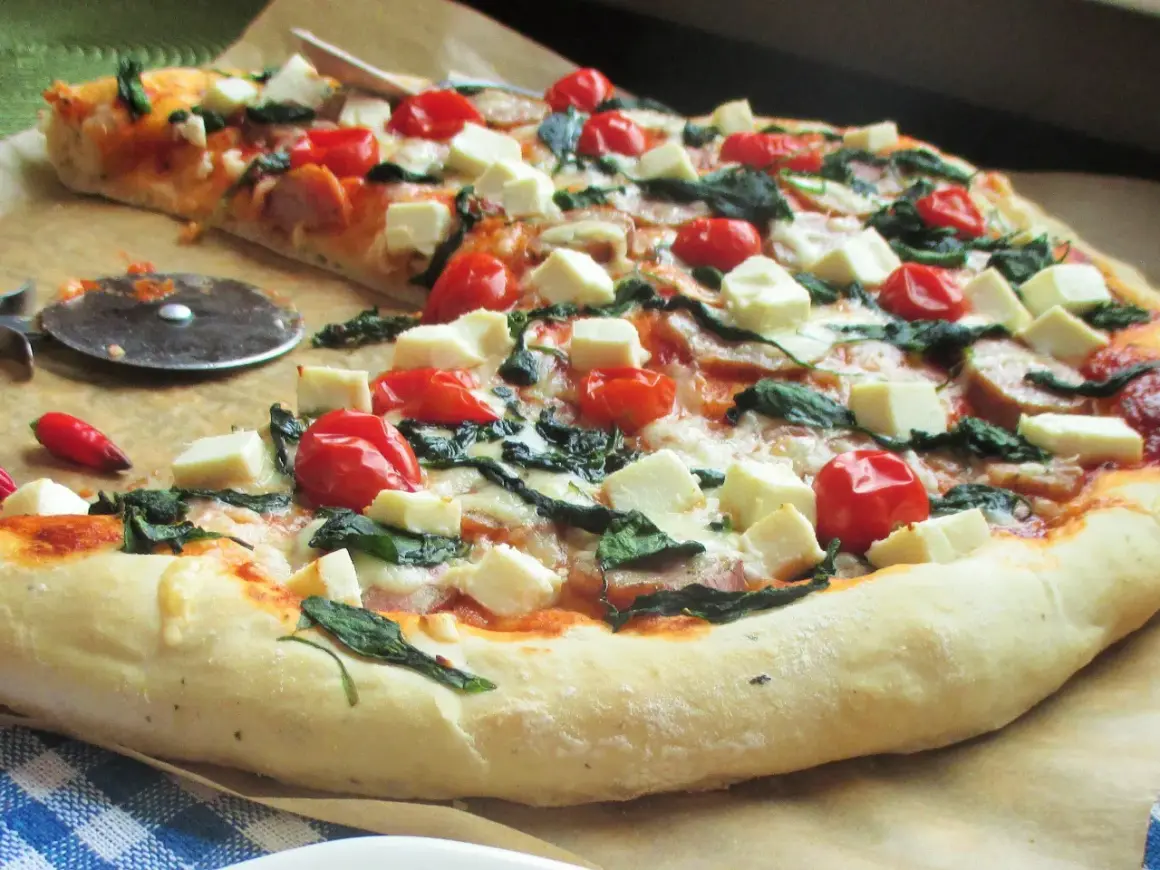 Pyszna pizza z fetą, pomidorkami koktajlowymi i szpinakiem, gotowa do pokrojenia.