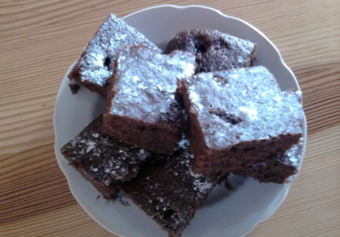 Czekoladowe ciasto z jednego jajka, pokrojone w kostkę i posypane cukrem pudrem, ułożone na talerzu.