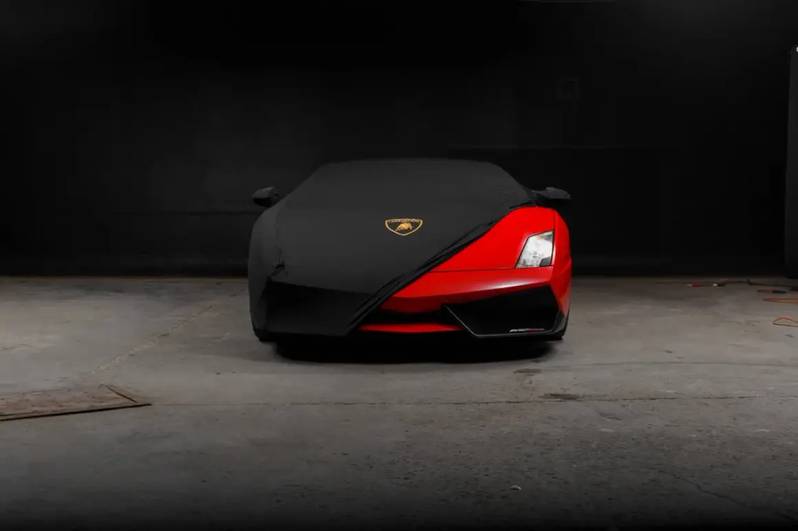 Czerwony supersamochód Lamborghini, być może najdroższe auto na świecie, częściowo przykryty czarnym pokrowcem z logo marki.