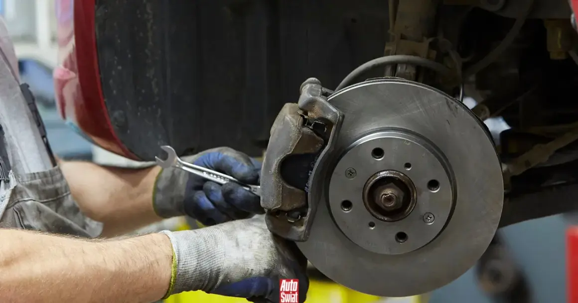 Mechanik w rękawicach dokręca śrubę przy budowie klocka hamulcowego.