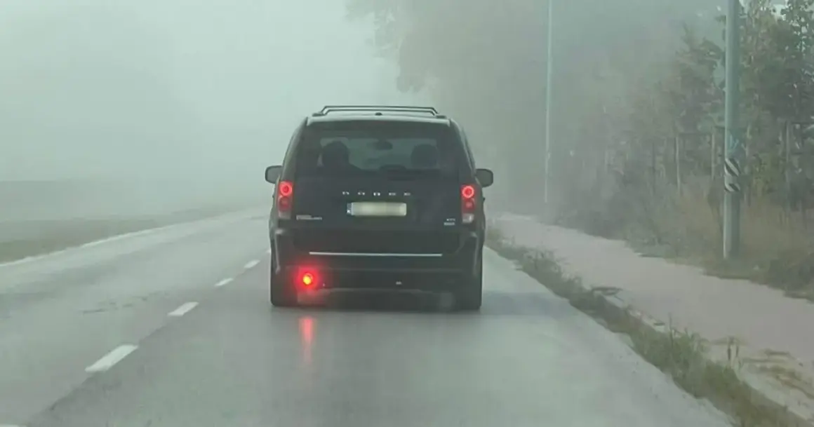 Ciemny van Dodge jedzie we mgle, włączone światła przeciwmgielne tylne poprawiają widoczność.