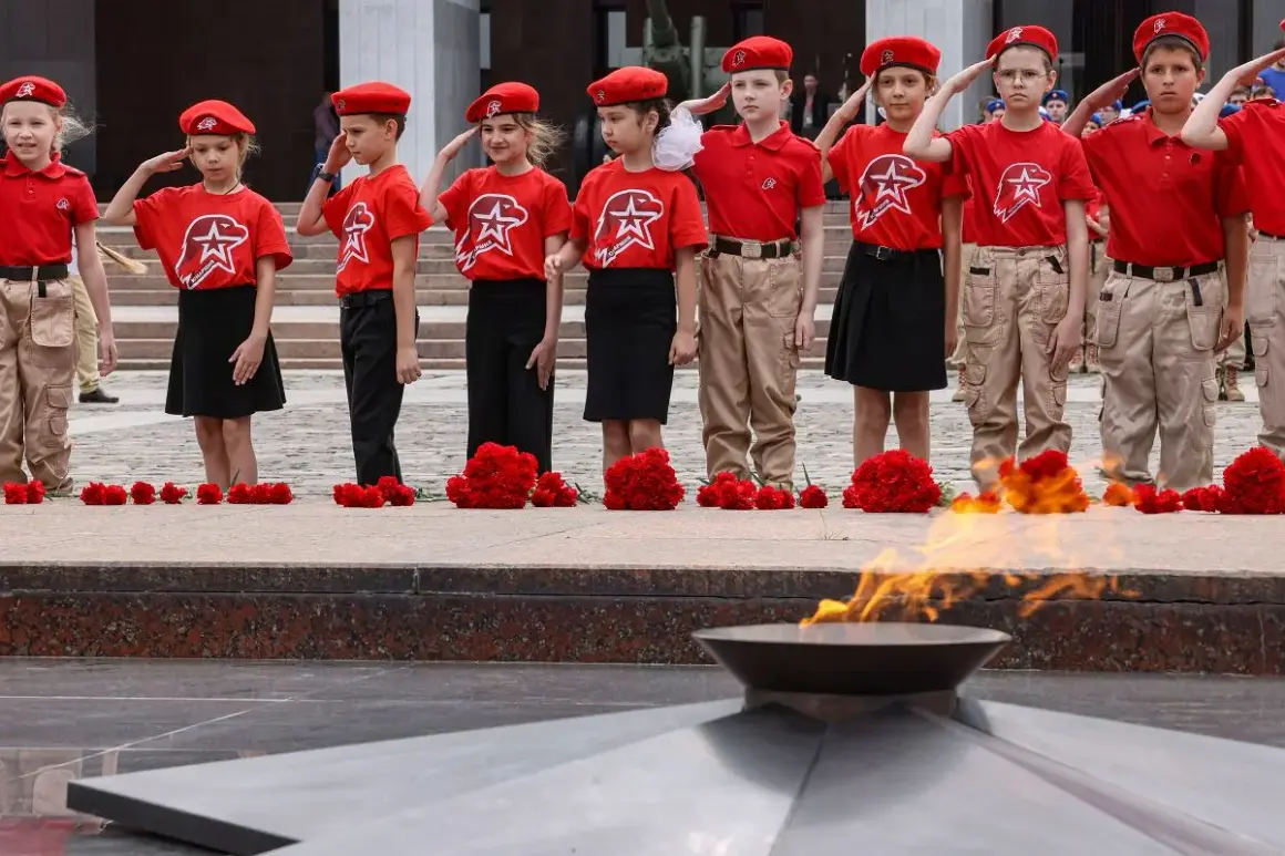 Dzieci w czerwonych beretach i koszulkach oddają hołd przy Wiecznym Ogniu. Utopijny i realny obraz rzeczywistości.