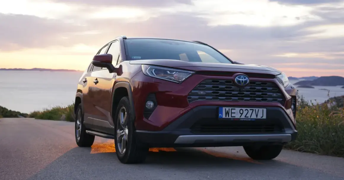 Czerwona Toyota RAV4 2.5 Hybrid na tle zachodzącego słońca nad morzem. Niskie spalanie to jej atut.