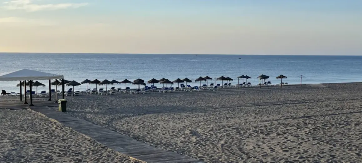 Playa marina de la torre con arena fina y tumbonas bajo sombrillas. El mar tranquilo se extiende hasta el horizonte.