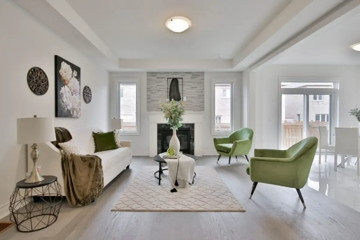 Salon moderne avec canapé blanc, fauteuils verts et cheminée. Le tapis et les coussins apportent une touche de blanc cassé.