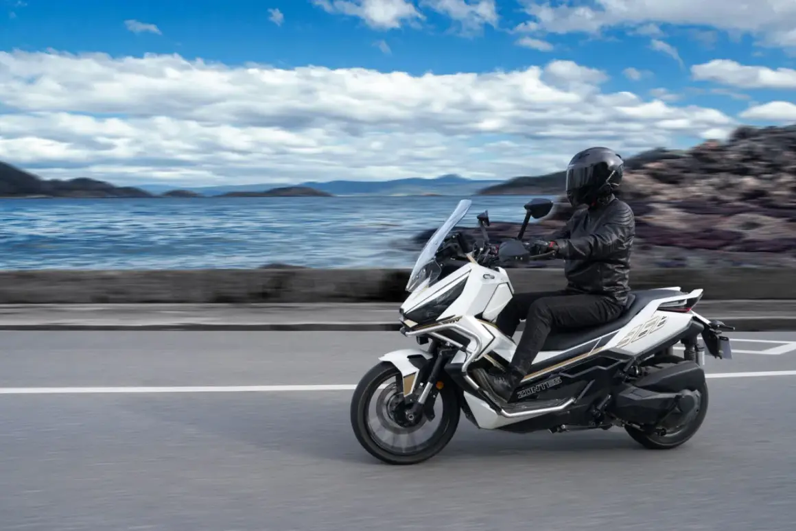Conductor en moto Zontes 368G blanca, con paisaje marino y montañas. ¡Las opiniones sobre esta moto son excelentes!