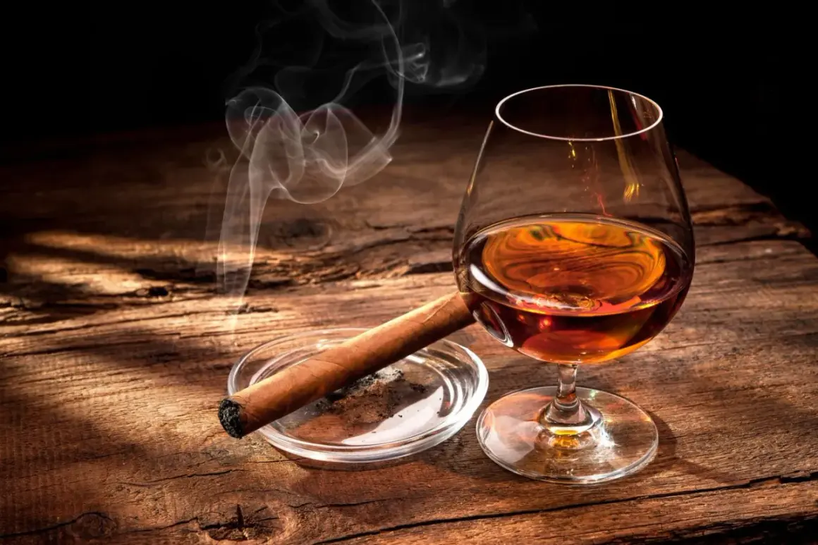 Ein Glas bernsteinfarbener Bourbon mit aufsteigendem Rauch von einer Zigarre auf einem Holztisch.