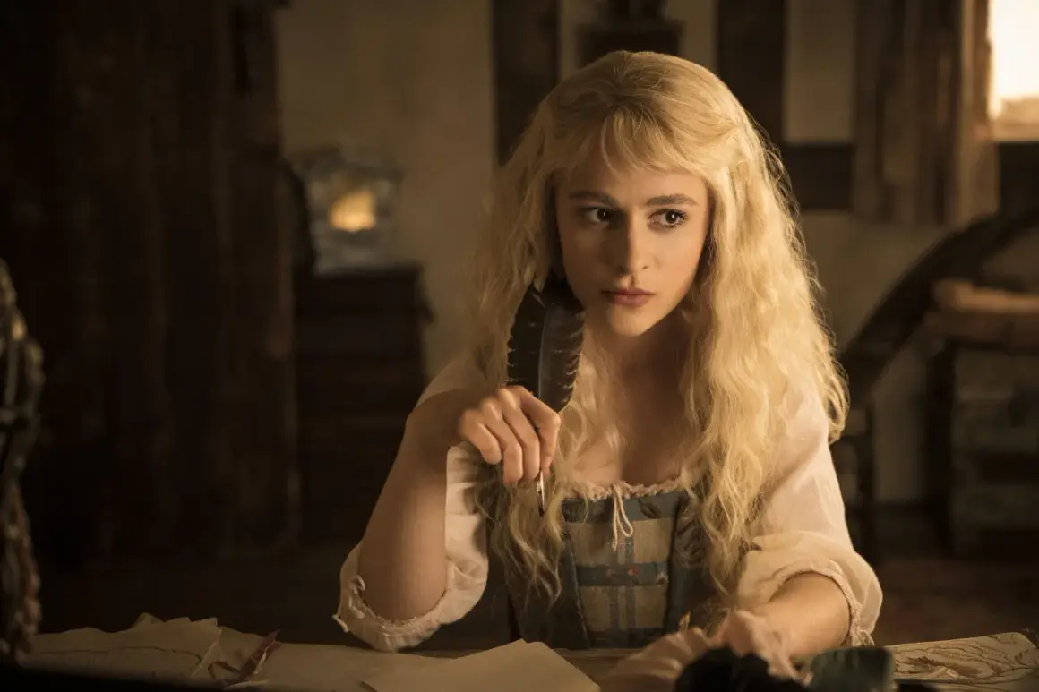Sophia Anne Caruso sitzt nachdenklich am Schreibtisch und hält eine Feder.