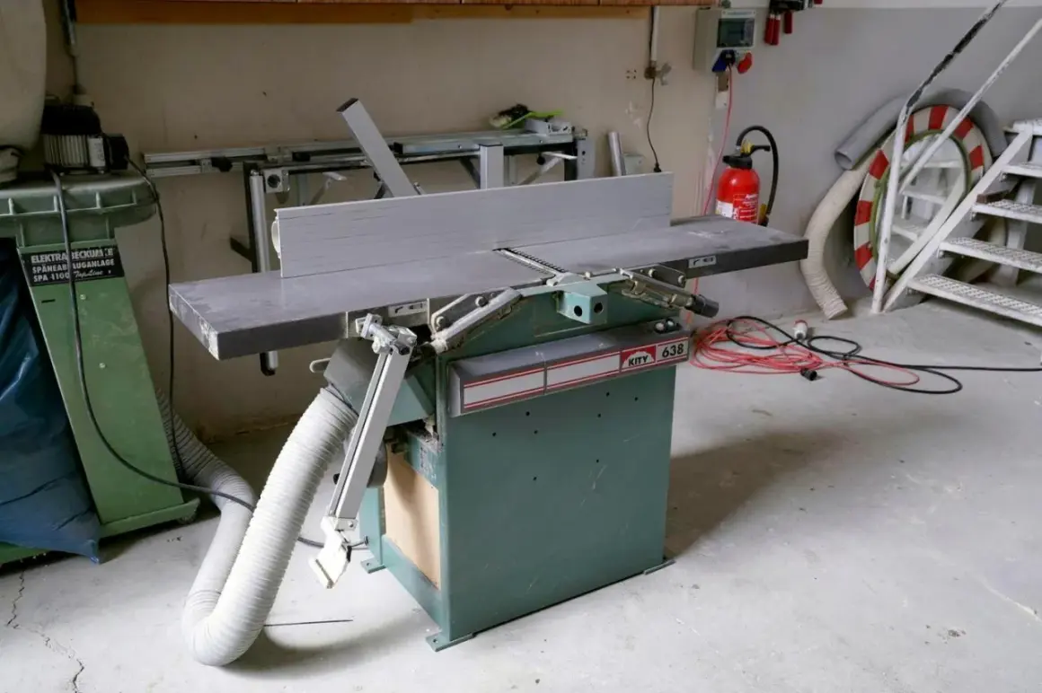 Détail d'une dégauchisseuse KITY 638 dans un atelier, avec un aspirateur à copeaux et des câbles électriques à proximité.