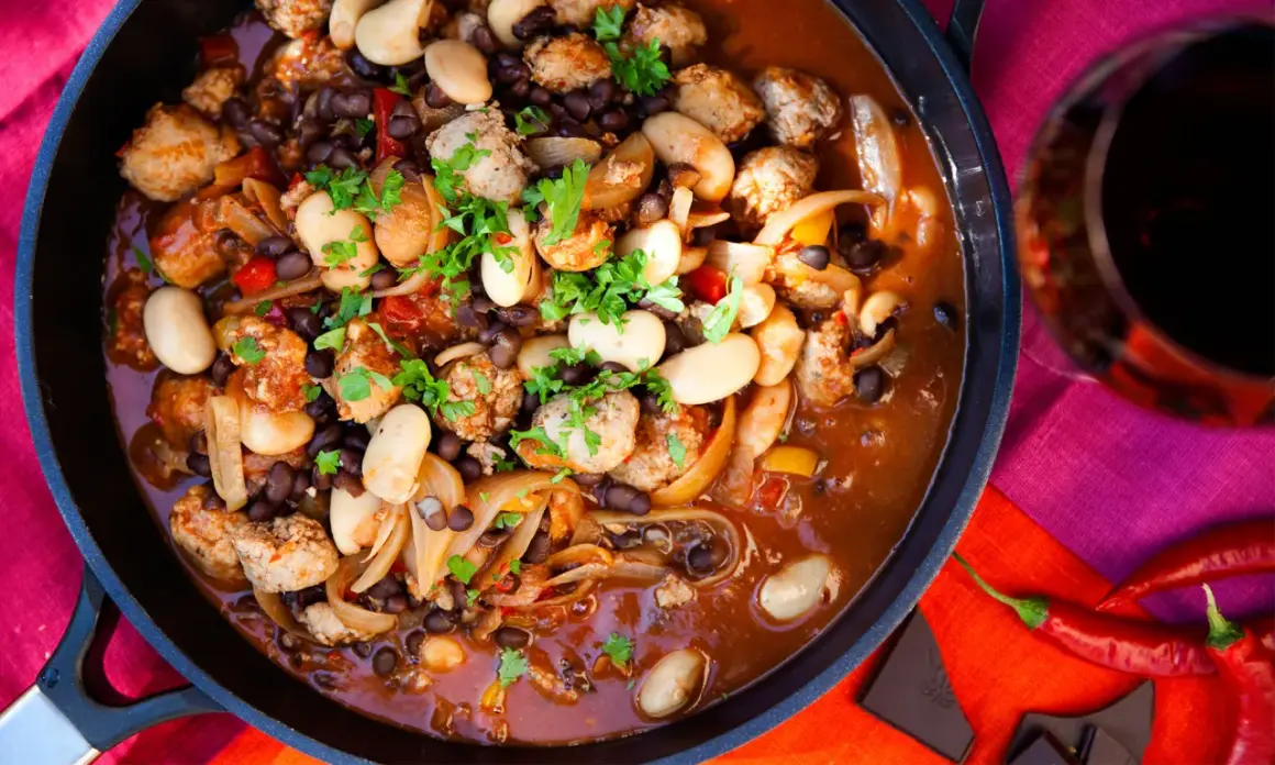 En mustig korvgryta med bönor och lök, perfekt för ett mysigt middagsrecept. Serveras med rödvin och chili.