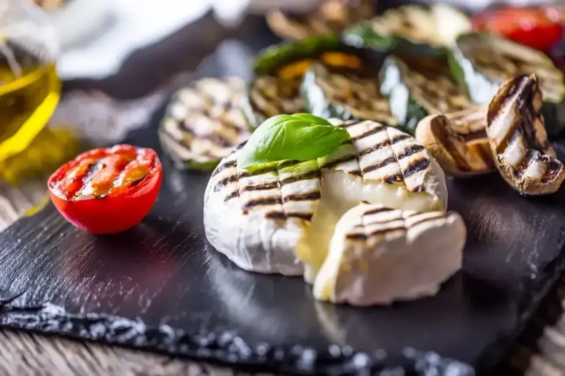 Ciepły camembert z grilla, z roztopionym wnętrzem, podany z grillowanymi warzywami i pomidorkiem.
