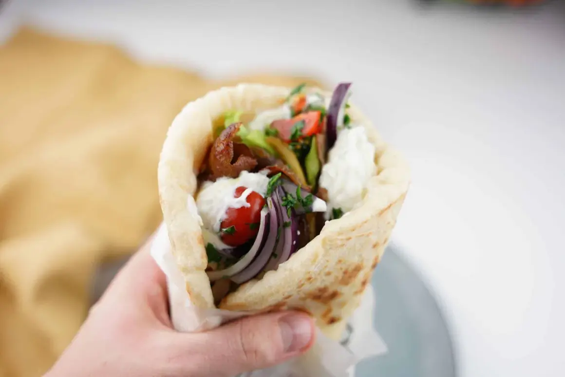 En hand håller en gyros med kött, grönsaker och sås. Perfekt för en supergod fredagsmat!