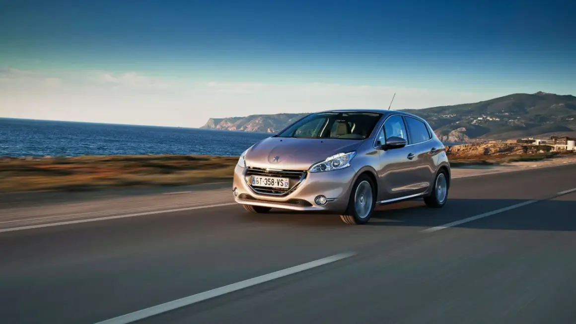 En Peugeot 208 kör längs en kustväg med havet till vänster och berg i bakgrunden. En perfekt bild för ett peugeot 208 test.