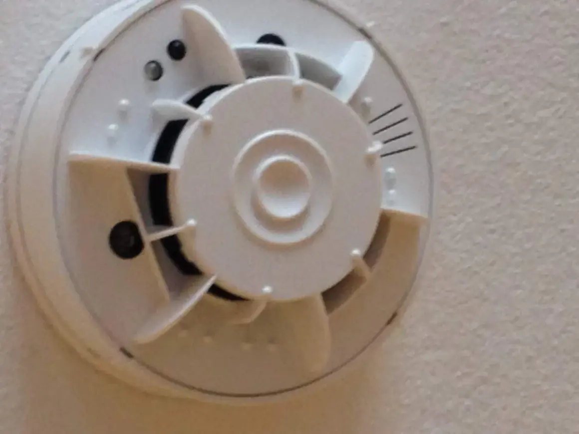 Ein weißer Rauchmelder mit integrierter Kamera, der an einer Decke montiert ist.