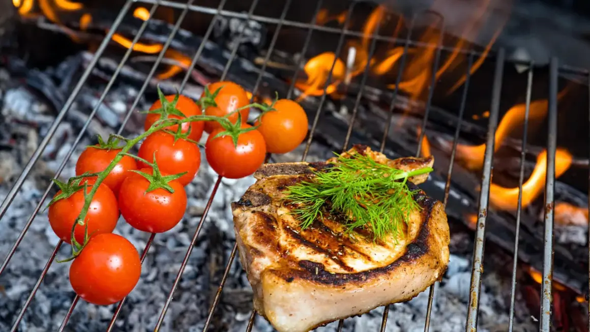 Ein saftiges Kotelett mit Dill und Kirschtomaten auf einem Grill im Haus. Flammen lodern im Hintergrund.