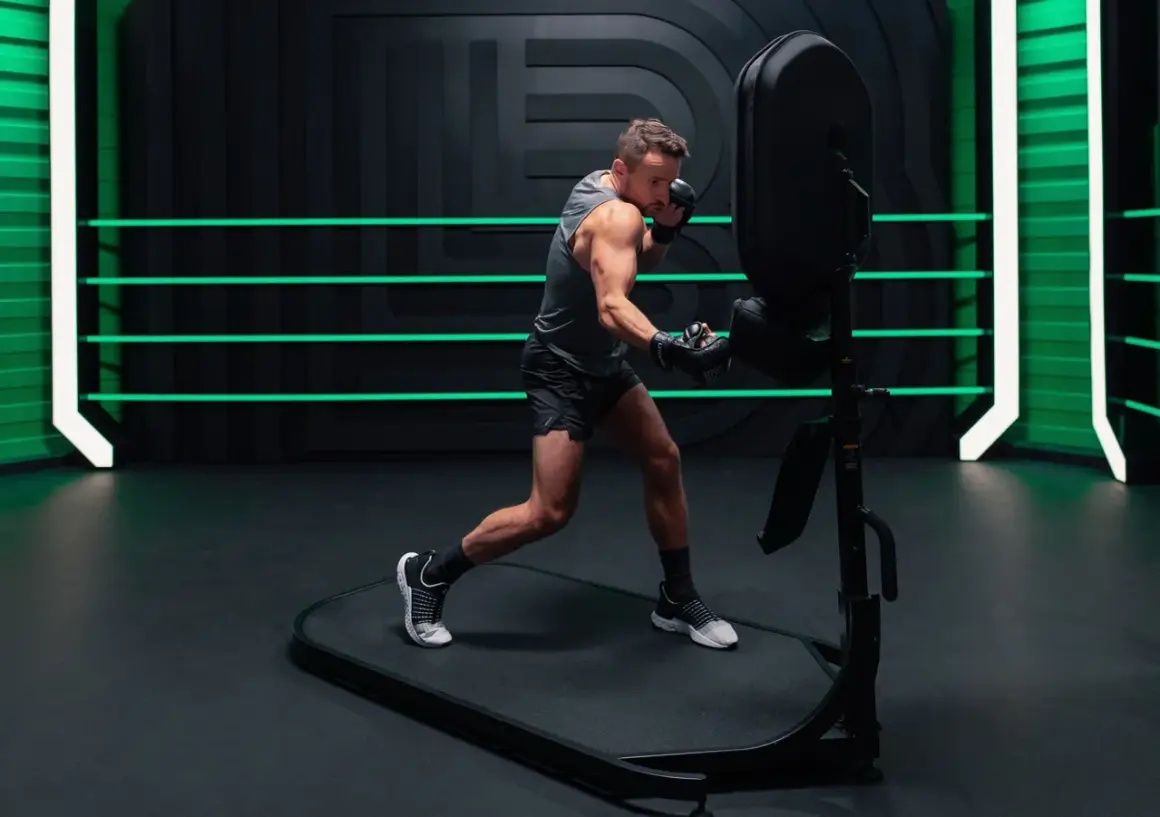 An orthodox fighter trains intensely, throwing punches at a boxing dummy in a modern gym with neon green accents.