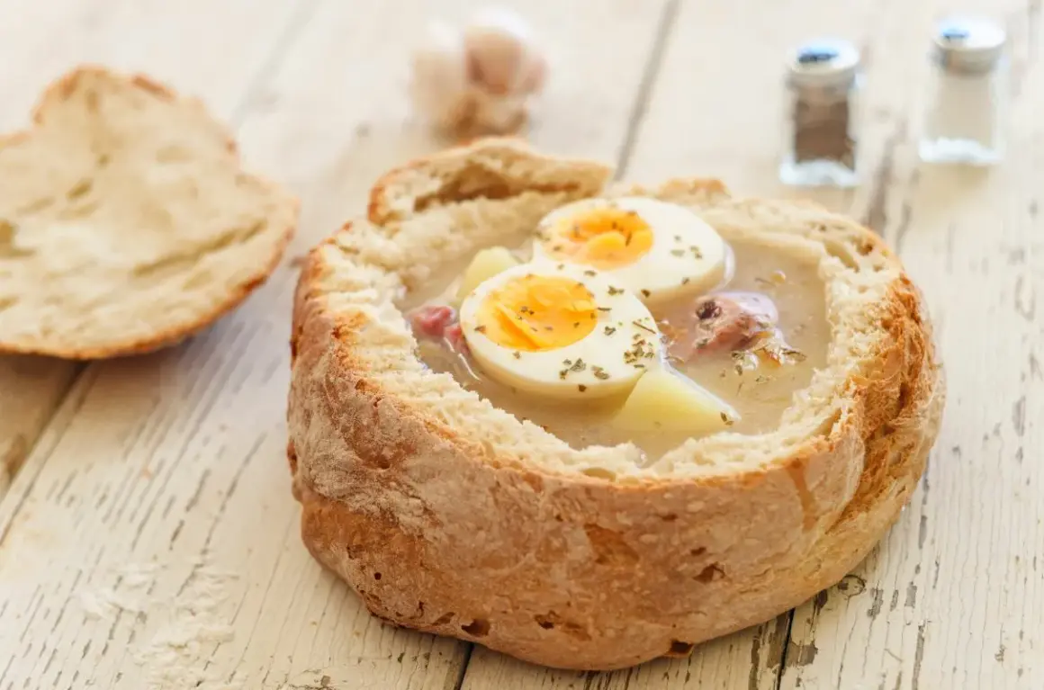 Gotowy zakwas na żurek w chlebie, z jajkiem i ziemniakami. Obok kromka chleba i przyprawniki.