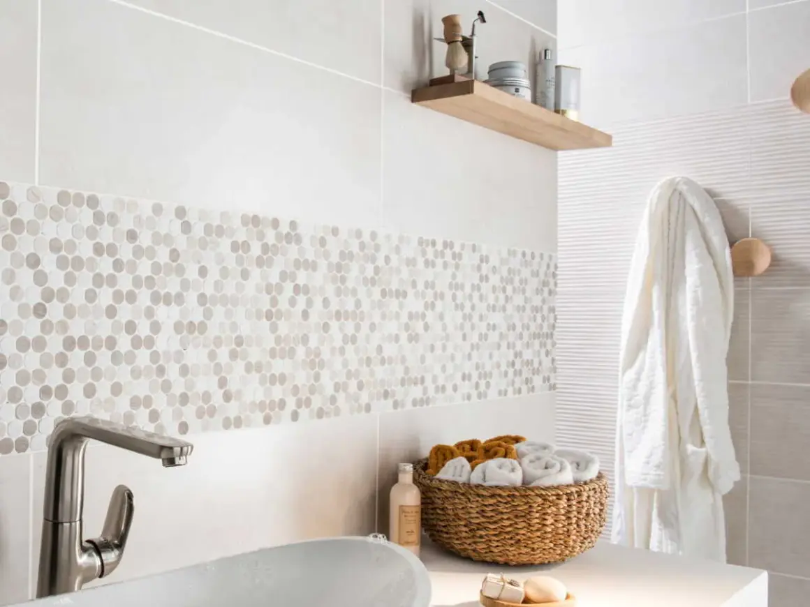 Détail d'une salle de bain moderne avec une bande de pose de faïence en mosaïque hexagonale. Un panier de serviettes et un peignoir blanc complètent la scène.