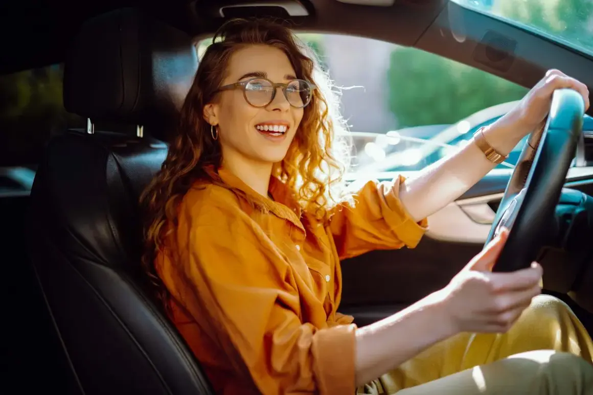 Uśmiechnięta kobieta w okularach za kierownicą. Wygodnie, bo to kategoria B, czym można jeździć.
