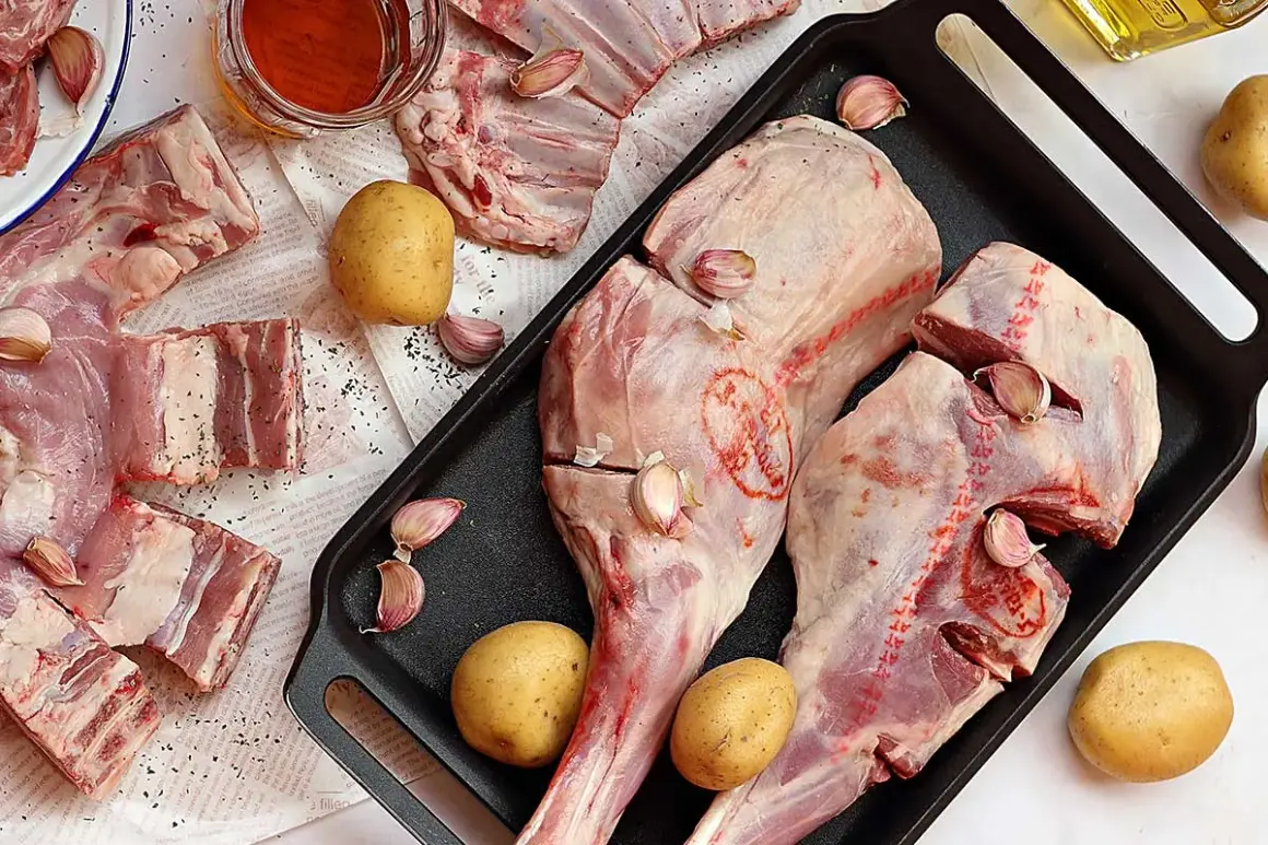 Pierna de cordero cruda con patatas, ajos y aceite de oliva, lista para asar.